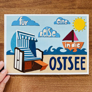 Gutschein in der digitalen Paper Cut-Methode erstellt. Die Illustration zeigt eine typische Szene in der Ostsee mit Strandkorb, Strand und Boot. Die Elemente sehen so aus, als wären sie mit Papier gebastelt.