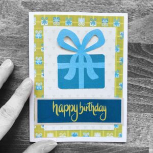 Eine Karte mit dem handgeschriebenem Titel "happy birthday" und einem Geschenk mit blauer Schleife aus Papier zu einem Blogbeitrag über analoge Kreativtechniken.
