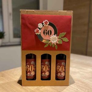 Drei Weinflaschen mit personalisiertem Etikett in einem Karton und mit Verzierungen aus Papier in einem Blogbeitrag über Geschenke zu einem runden Geburtstag.