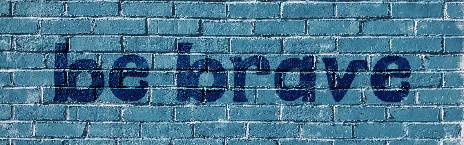 Quote "be brave" auf einer blau gefärbten Steinmauer in einem Blogbeitrag über das erste Mal skateboarden