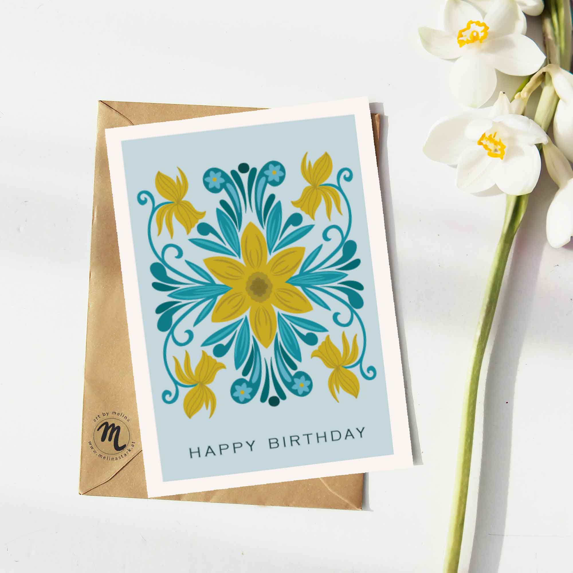 Mock-up einer Grußkarte mit einer Illustration einer Narzisse im symmetrischen Folk art-Stil. Daneben liegt eine weiße Blume. Unter der Karte liegt ein braunes Kuvert.