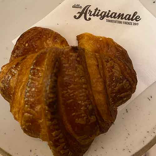 Ein Croissant liegt auf einem Teller. Auf der Serviette steht der Name des Lokals.