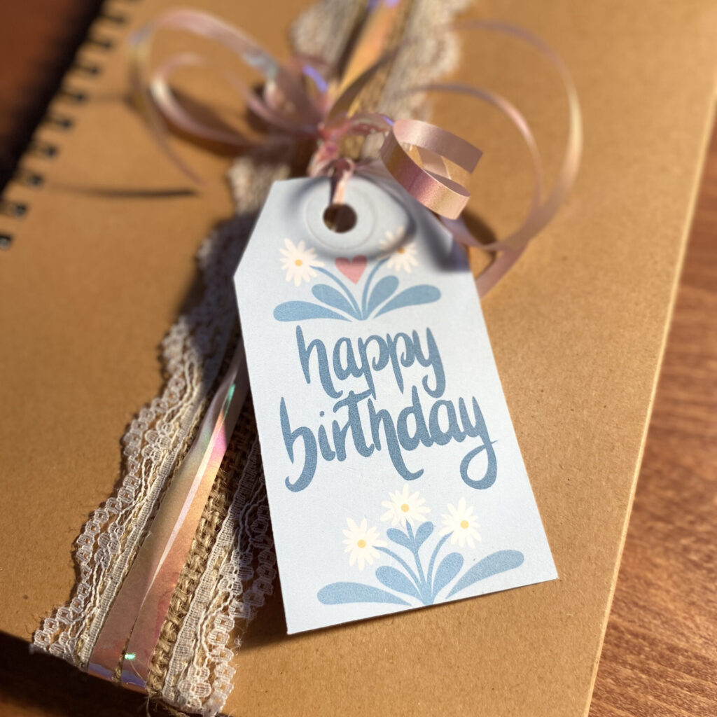 Ein Notizbuch mit Geschenksband und Geschenkanhänger, auf dem "happy birthday" steht.